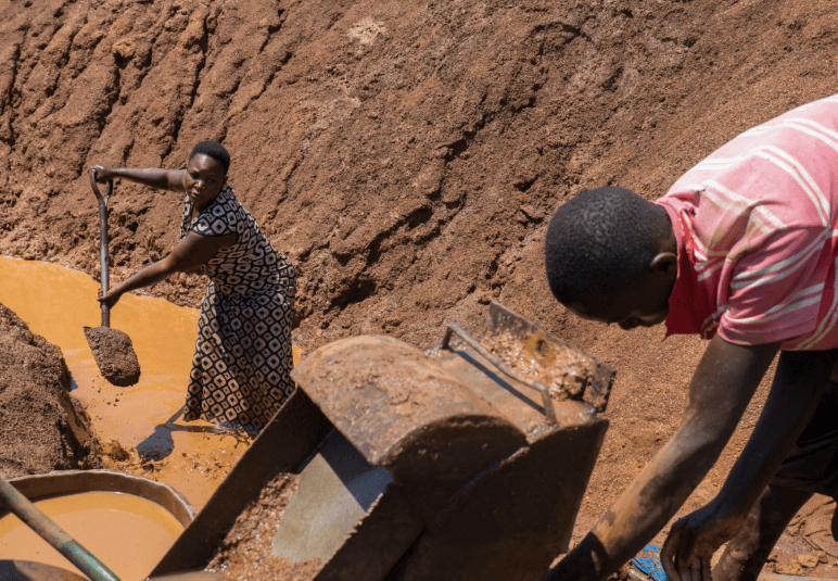 Woman shoveling mud and man working with metal equipment at an artisanal mining site.