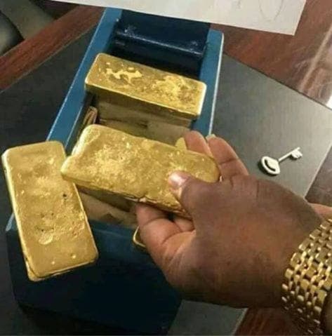 Hand with gold watch holding a gold bar over a box of gold bars.