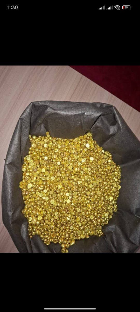 A dark grey bag filled with small, shiny gold nuggets on a wooden surface.